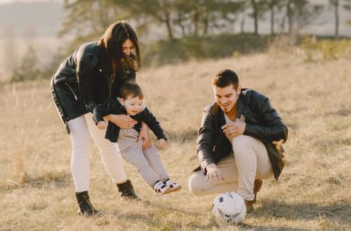 A happy family playing with a soccer ball in a grassy field on a sunny day.